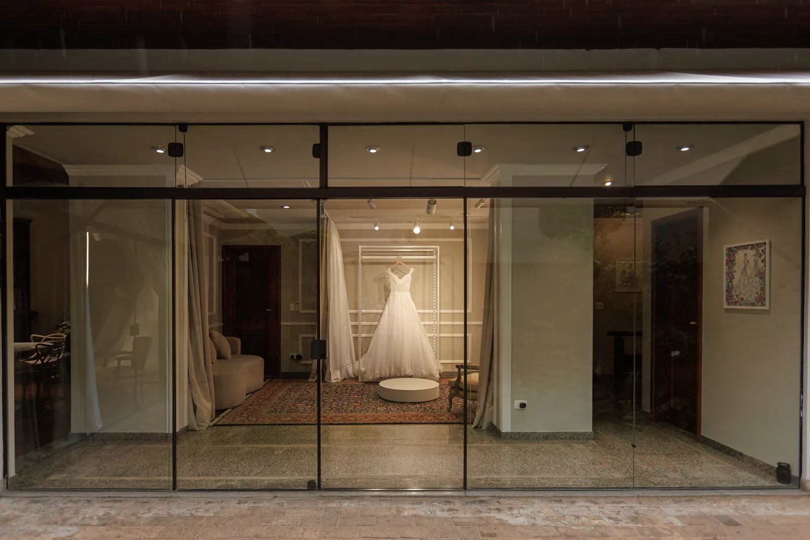 A fachada de vidro da Casa ao entardecer, com o vestido iluminado na vitrine.